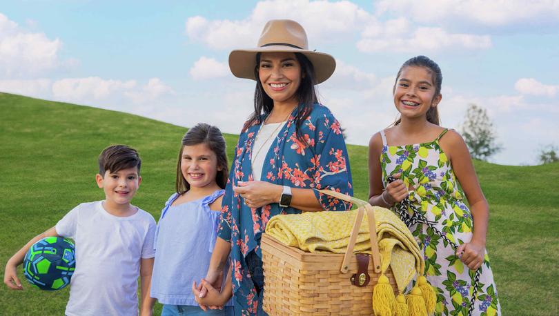 Stylish mom carrying a picnic basket, blanket with two young girls and boy with a ball
