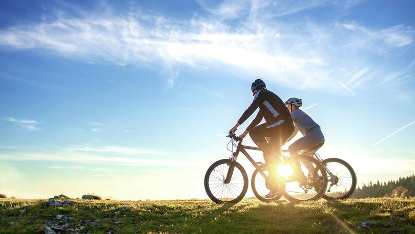 Silhouette of couple on bikes at sunset, open grass trail and blue skies.