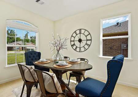 Staged home with large wall clock, small round wooden table with placesettings, and mismatched blue and white chairs