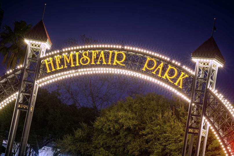 San Antonio, Texas Hemisfair Park sign lit up at night with the words Hemisfair and park in yellow and the structure holding it lined with large-bulb lights