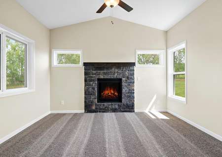 Photo of four-season porch room with windows on all walls, a stone surround fireplace, carpeting and a ceiling fan.