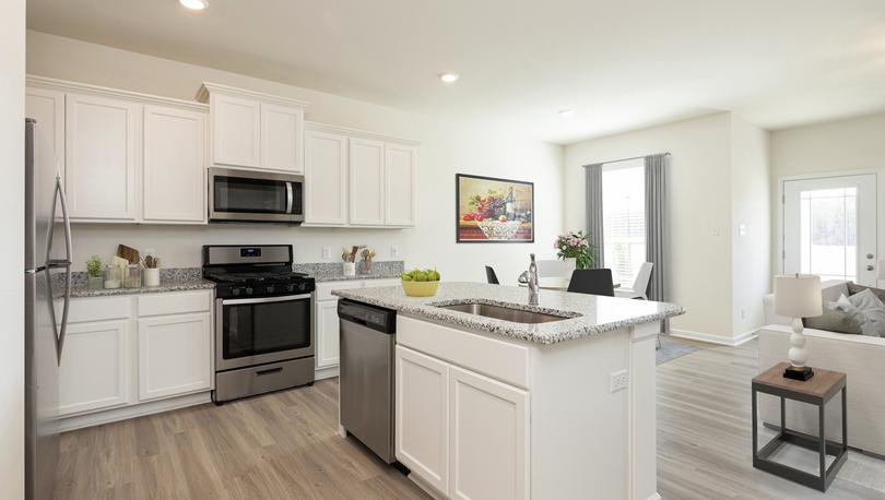 Open-concept kitchen, dining and living room with lots of natural light featuring pale plank flooring, white cabinets, stainless appliances, gray granite counters, recessed lights.