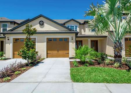 Exterior view of the Calabria floor plan model that has grass, bushes and a small palm tree in the front yard.