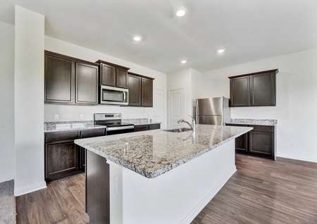 Rio kitchen with recessed lights, large granite kitchen island, and brown custom cabinets
