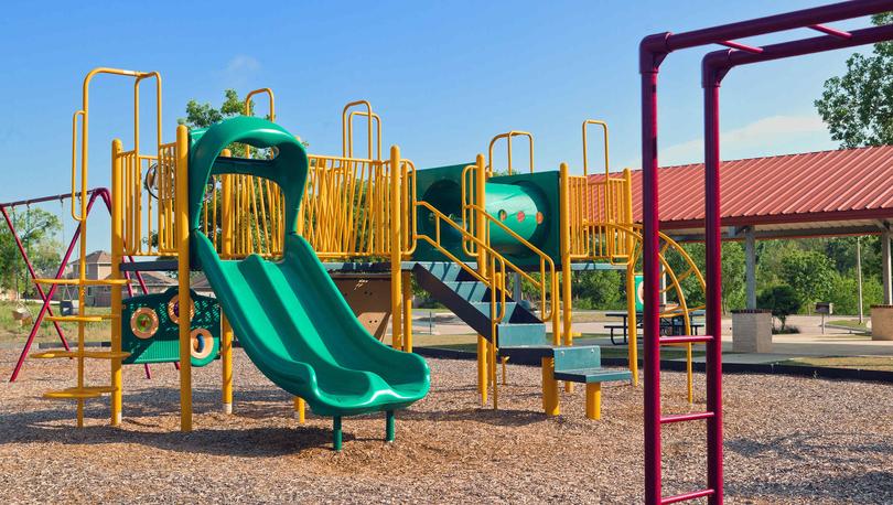 Bunton Creek new home community children's playground with green slides, yellow climbing equipment, and wood chips