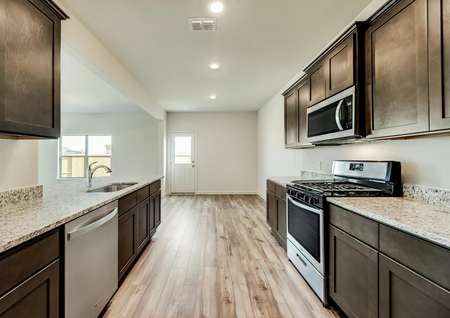 The kitchen has light flooring and brown cabinetry and is open to the dining room.