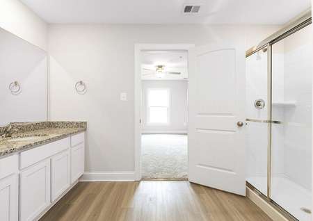 Photo of the primary bathroom with white cabinets, plank flooring, granite counters and an oversized walk-in shower.