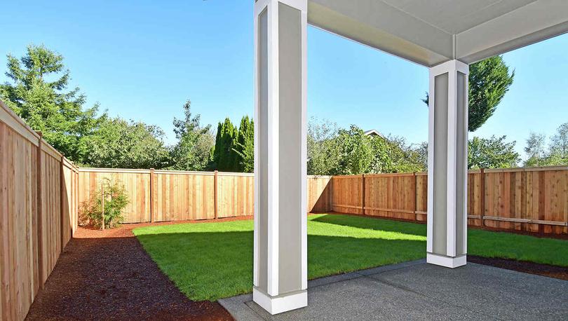 Photo of a fenced back yard with green grass from underneath a covered back patio.