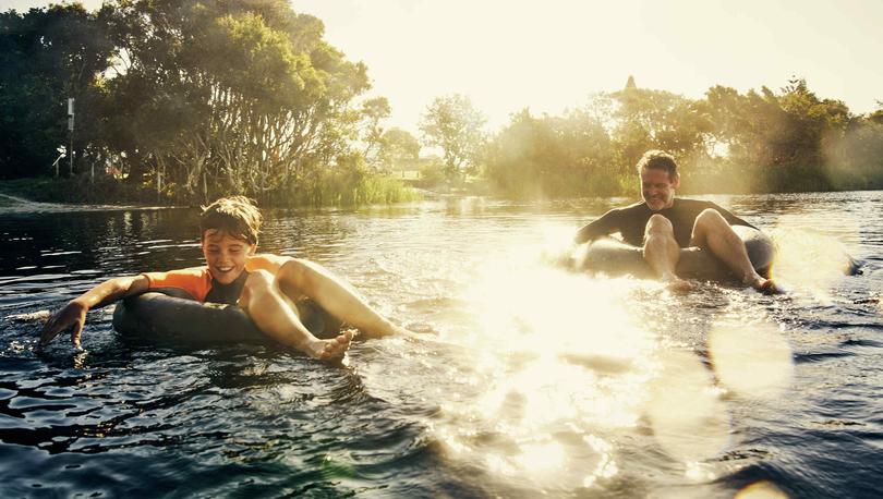 Father and son drifting down river on black intertubes with trees in the background