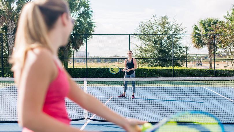 Two ladies smiling and playing tennis on a sunny day. 