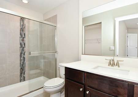 Photo of primary bathroom with dark cabinets and glass door on shower with decorative tile wall.