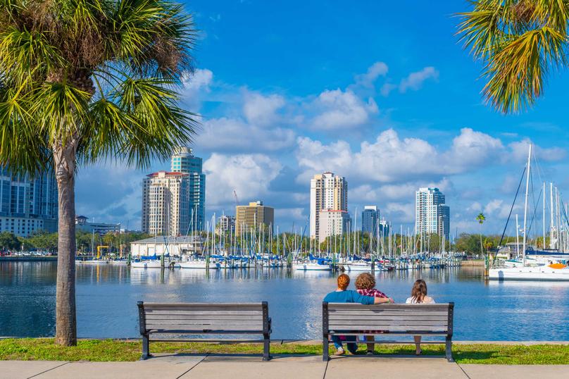Tampa St. Petersburg bay with people on bench, palm trees, and skyscrapers in the background