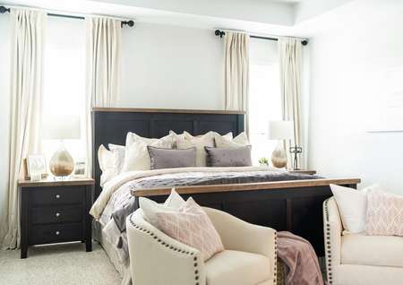 Bedroom with plush pillows and blankets and two chairs for seating