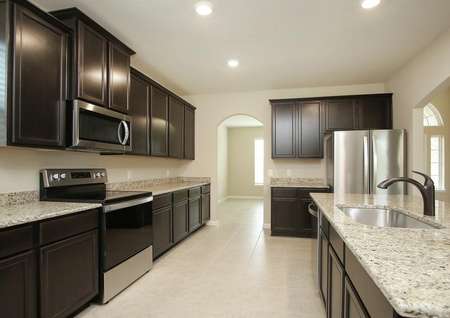 Spacious kitchen with close up of granite counters, antique bronze faucet, espresso cabinets,tile floor, stainless appliances, recessed lighting looks into formal dining and foyer.