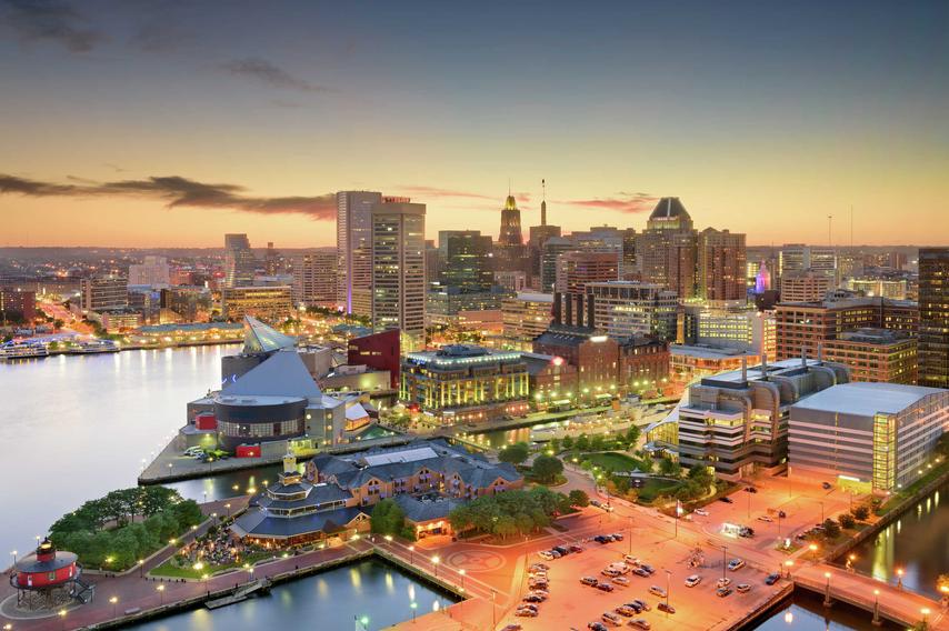 Baltimore, Maryland Inner Harbor and downtown Skyline showing numerous building's windows lit up and the sun setting in the horizon