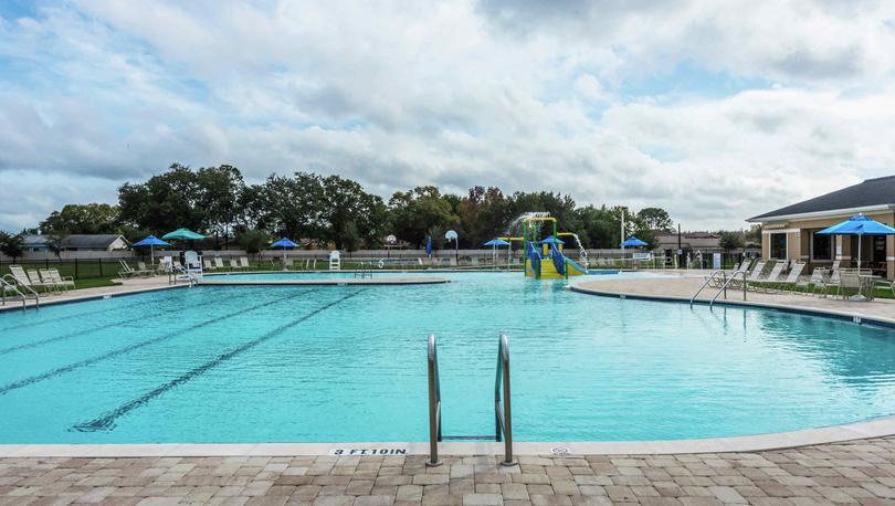 The pool of the Poinciana community that has brick pavers around it and a water slide on the far side of the pool.