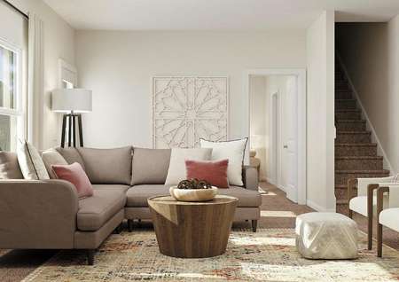 Rendering of the
  living room in the Driftwood with a large window, tan walls and carpeted
  flooring. The room is decorated with a large sectional, two white armchairs
  and a round coffee table.