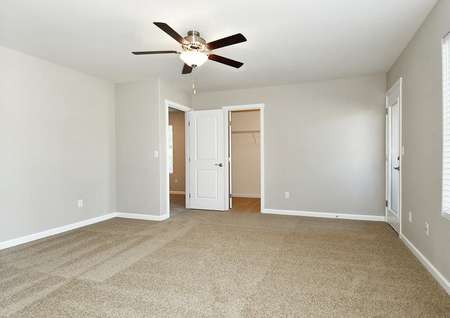 Large master bedroom with carpet, ceiling fan, window and door to balcony.