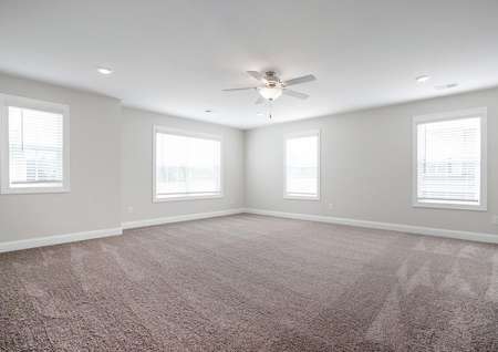 Large master bedroom with ceiling fan, carpet and a lot of windows.