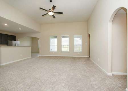 Carpeted living room with three windows, ceiling fan with light, and access to the kitchen in the Leland model
