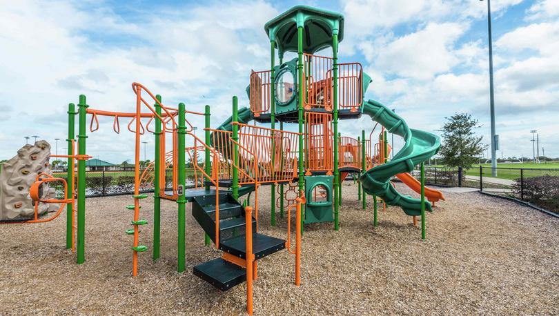 A playset that is orange and green in the Poinciana community playground area that is gated.