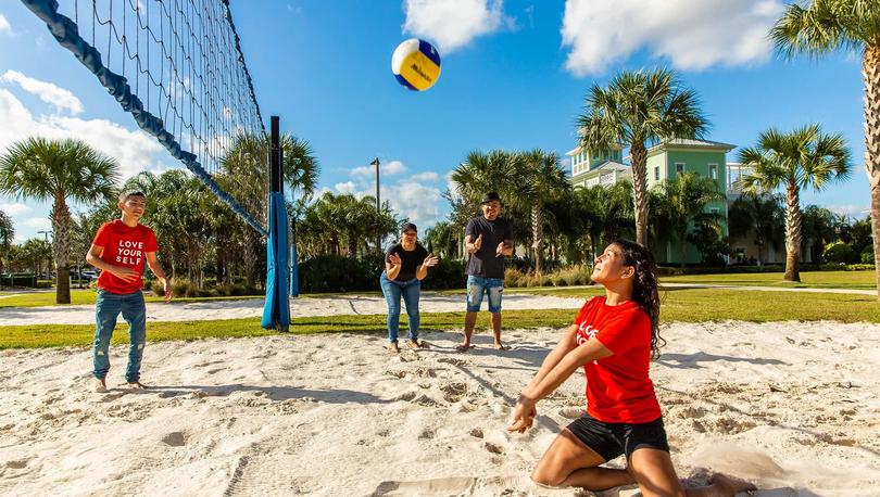 Family of four smiling and playing sand volleyball. 