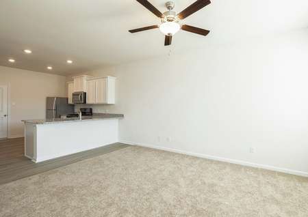 Living room with carpet and ceiling fan looks to breakfast bar and kitchen with white cabinets