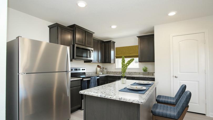 Staged kitchen with dark brown cabinets, stainless appliances, island with two barstools and window over the sink, pantry door visible.