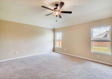 Spacious master bedroom with two windows, ceiling fan, two-tone paint and carpet in neutral palette.