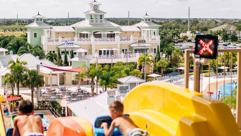 Two boys racing down the water slides of a resort's water park. 