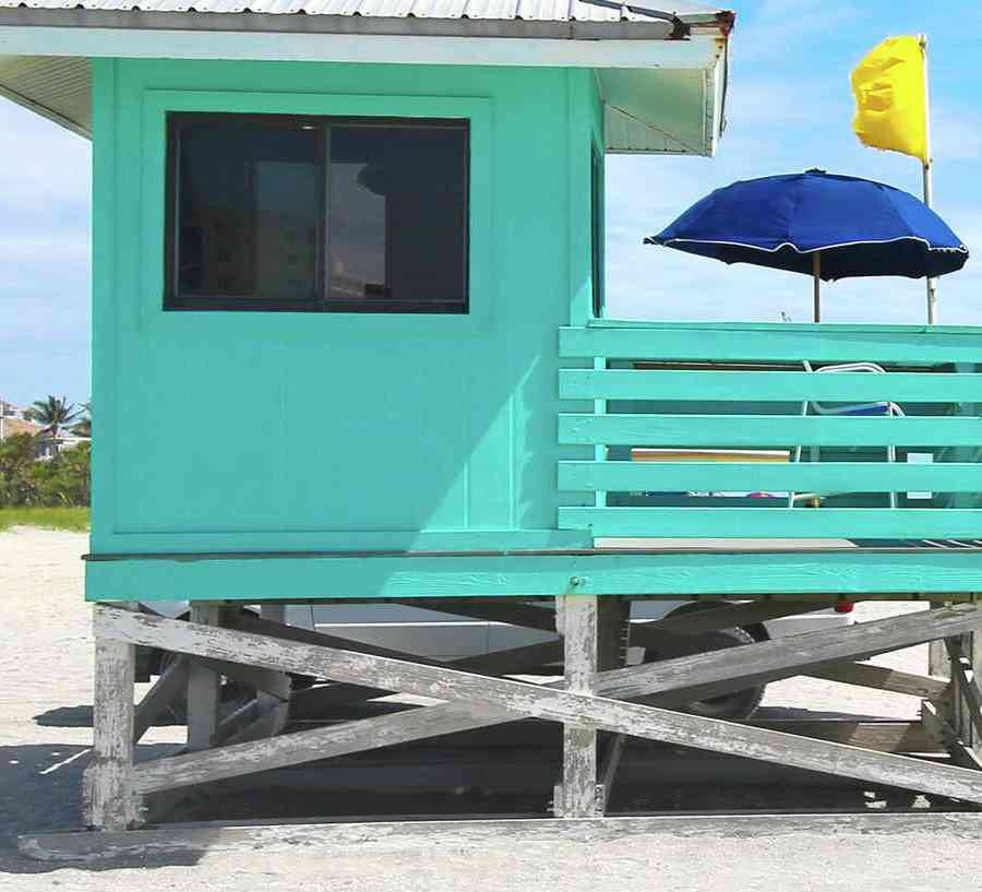 Sarasota, Florida turquoise lifeguard station with blue sun-umbrella, white sandy beach, and turquoise waters
