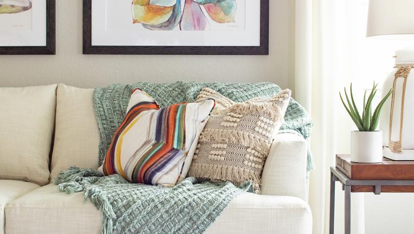 Staged living room with couch that has throw pillows and decorations hanging above it. 