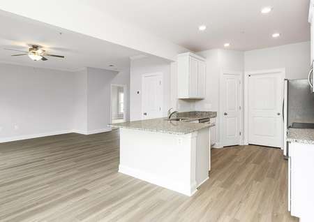 Open kitchen, dining and living room with plank flooring, white cabinets, recessed lighting and a ceiling fan.