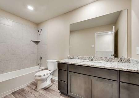 Ozark bathroom with large granite vanity, wood cabinetry, and shower/tub combo