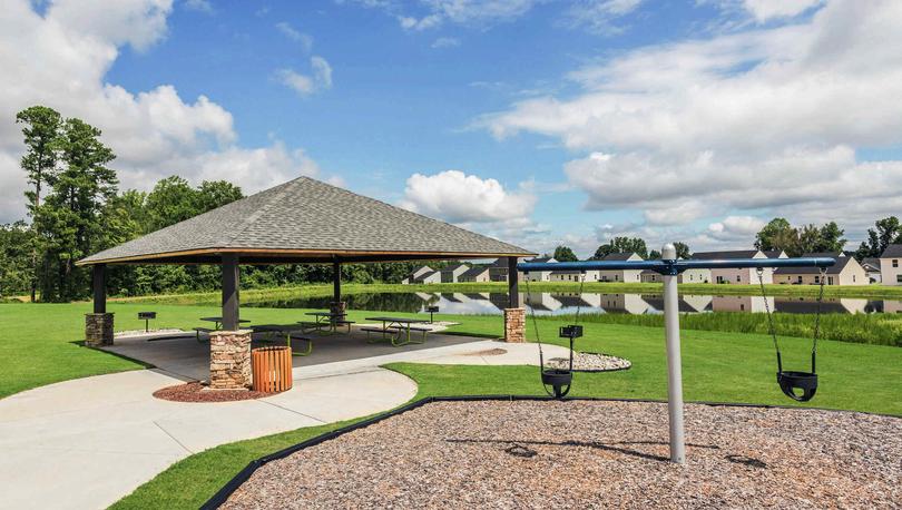 Community play area with a swing set for young kids and a covered pavilion with benches in the shade beneath it.