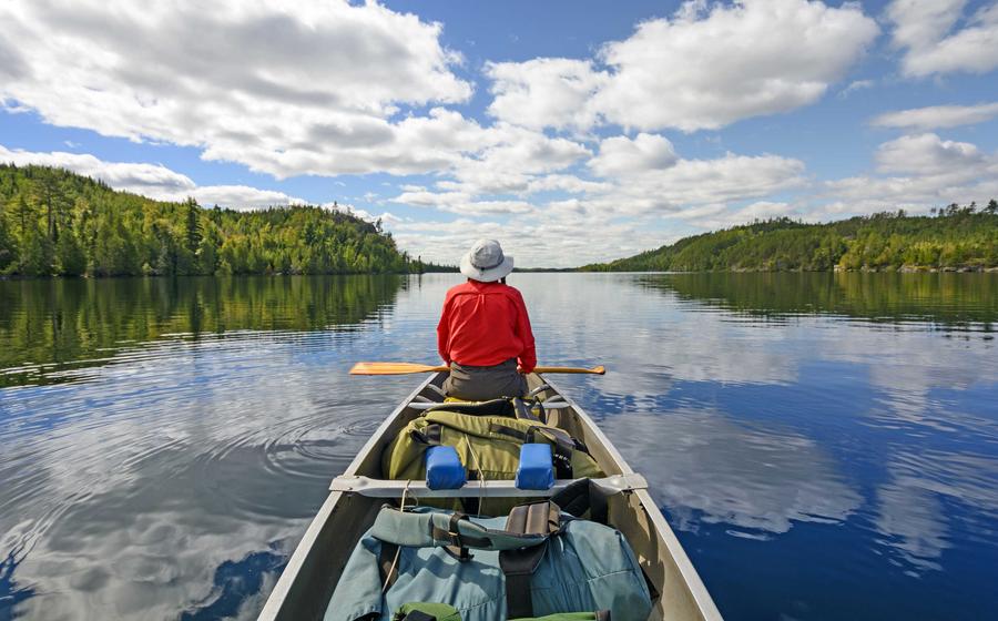 Person canoeing on serene lake surrounded by trees