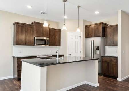 Photo of kitchen with brown cabinets with crown molding, dark gray countertops, stainless steel appliances and decorative light fixtures.