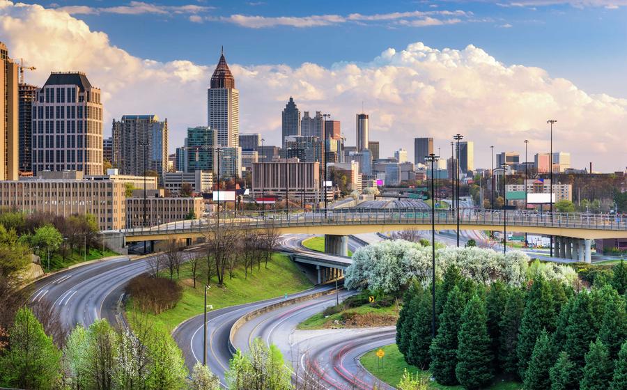 Atlanta, Georgia Downtown Skyline featuring numerous skyscrapers and office buildings, cars driving on the freeways, and blue skies with white clouds