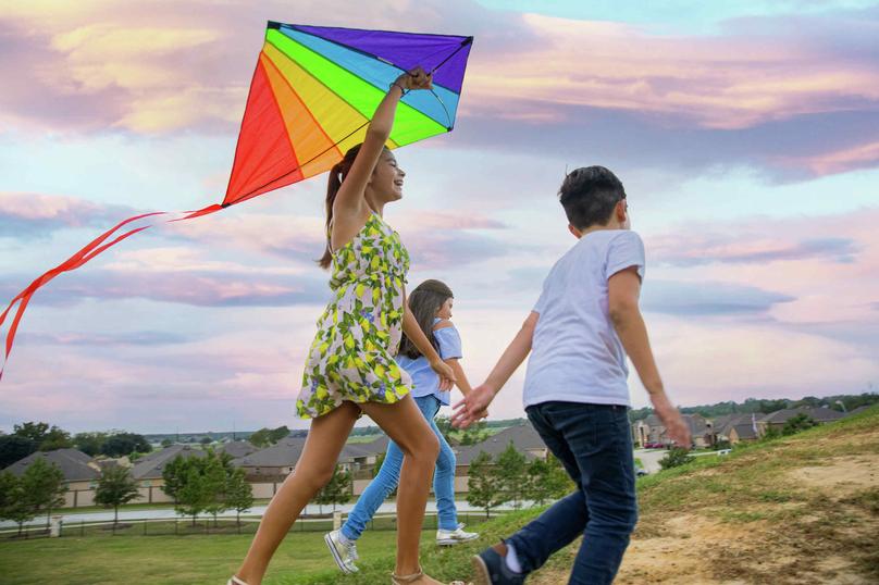 Three kids running with a kite in a park.
