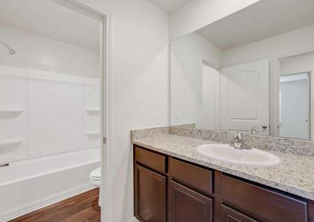 The Rio model home's second bathroom with granite countertops, dark brown cabinetry and shower and tub combo 