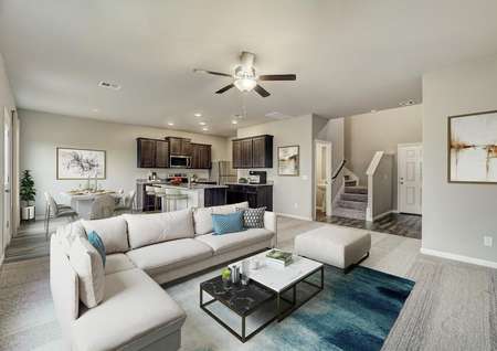 Staged living room with a light tan couch and kitchen.