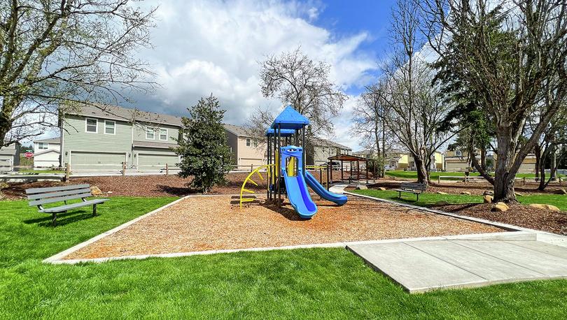 Photo of a neighborhood park with a playground, bench and trees.