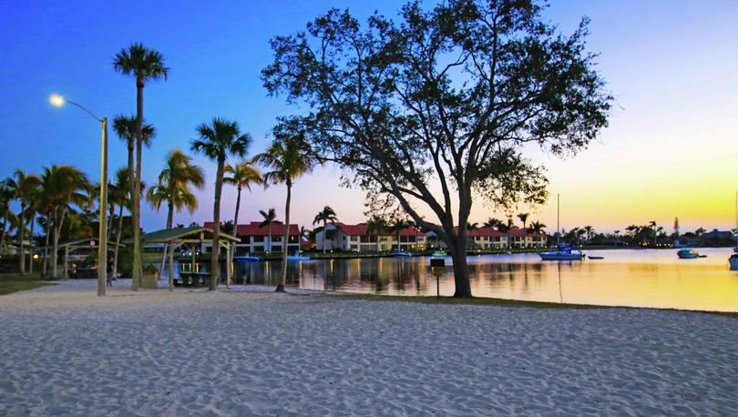 Cape Coral, Florida beach park with white sands, palm trees, and calm waters at sunset