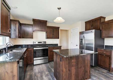 Photo of a spacious kitchen with dark brown cabinets and dark gray granite counters, an island, and stainless steel appliances.