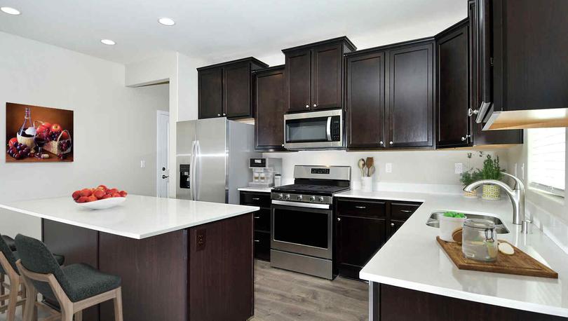 Pearl model home kitchen with white travertine counters, stainless steel appliances, and dark custom wooden cabinets