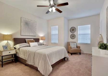 Fully furnished master bedroom with carpet flooring, two windows and a ceiling fan.