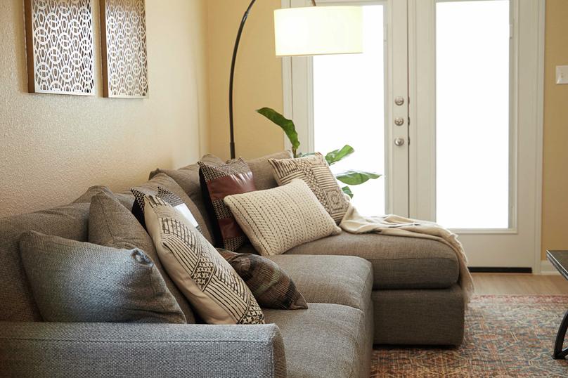 A living room decorated with a comfortable, gray couch with tan accents, a large floor lamp, and French doors that lead to the large backyard.