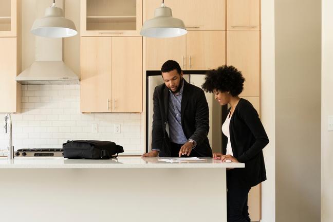 An agent and his client review paperwork at the kitchen island in an empty house.