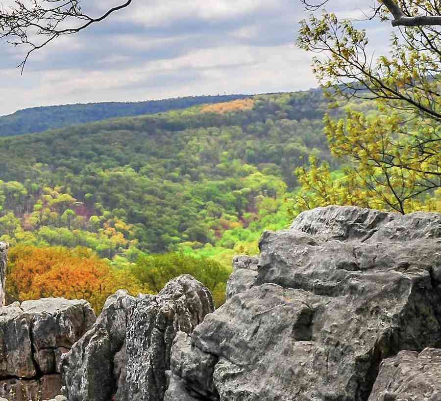 Maryland Appalachian Mountains during Autumn showing woman sitting on rocky outcropping, trees that have lost their leaves, and rolling hills of vegetation