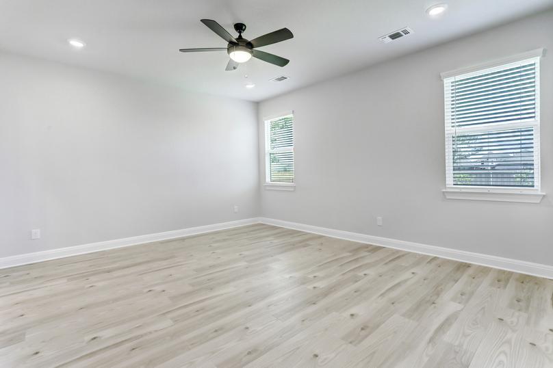 Expansive master bedroom with wood flooring, a ceiling fan, and two windows to allow natural light to flow in.